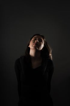 Moody studio portrait of a young woman with closed eyes and dark background.