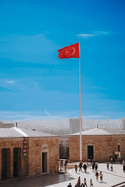 A red flag flying over a city with people walking around