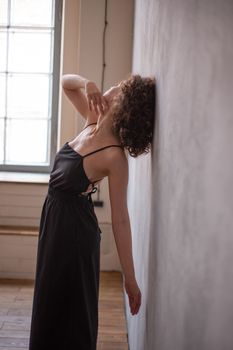 Woman in a black dress with curly hair posed against a wall indoors.