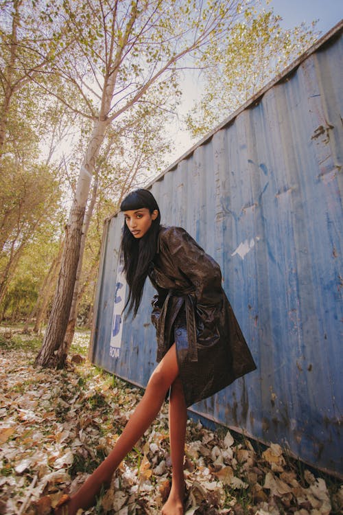 A woman in a coat and tights posing near a blue wall