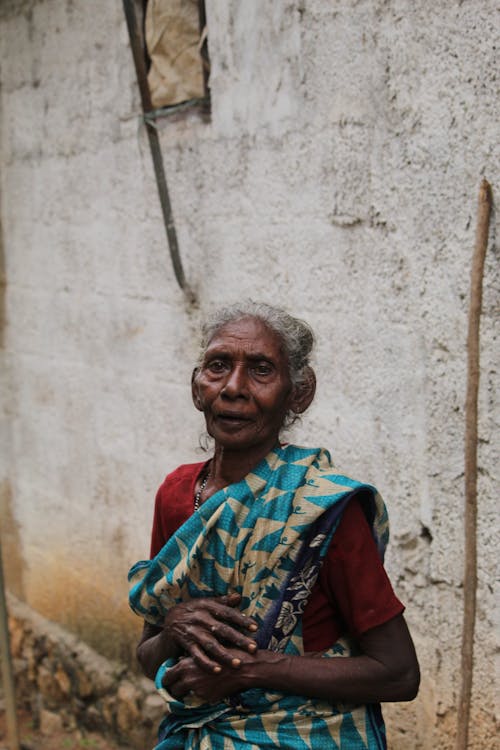 An old woman in a sari standing outside a house