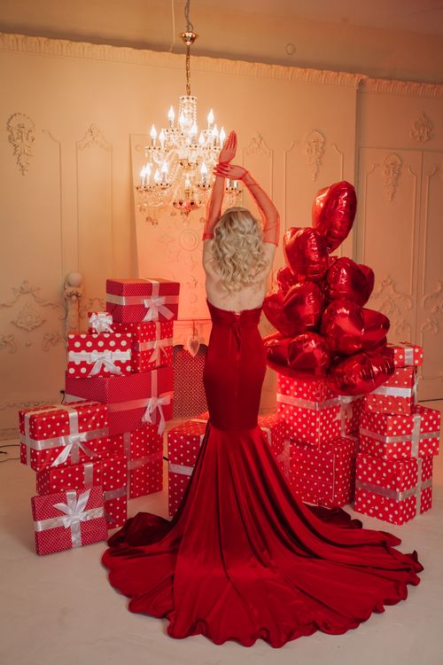 Free Blonde woman in red gown stands among red gift boxes and balloons, under chandelier. Stock Photo