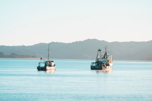 Two boats are in the water near a mountain