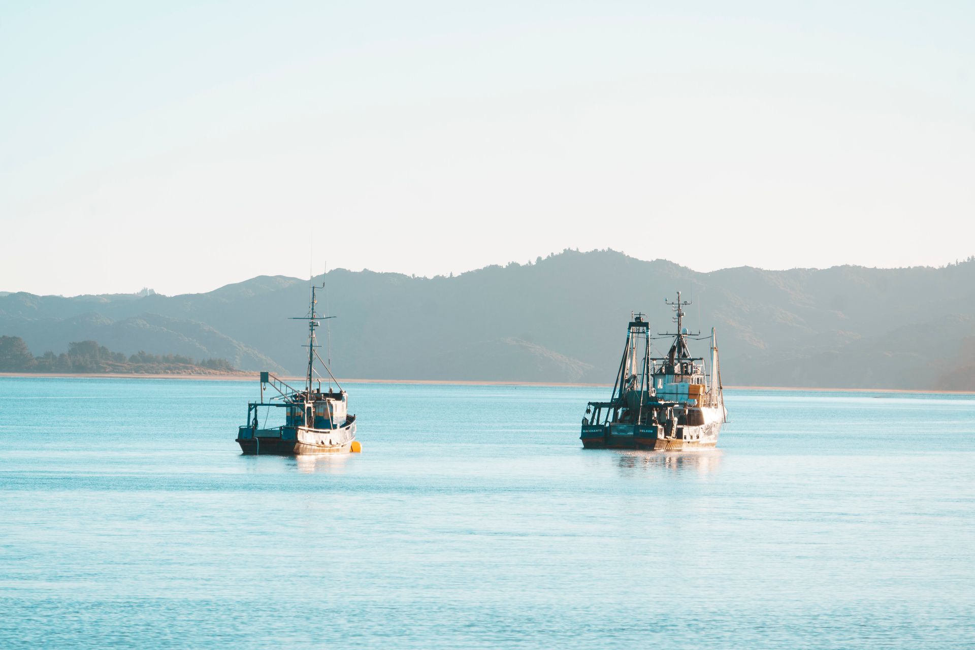 Peaceful scene of fishing boats floating on a calm bay with distant mountains under clear skies.
