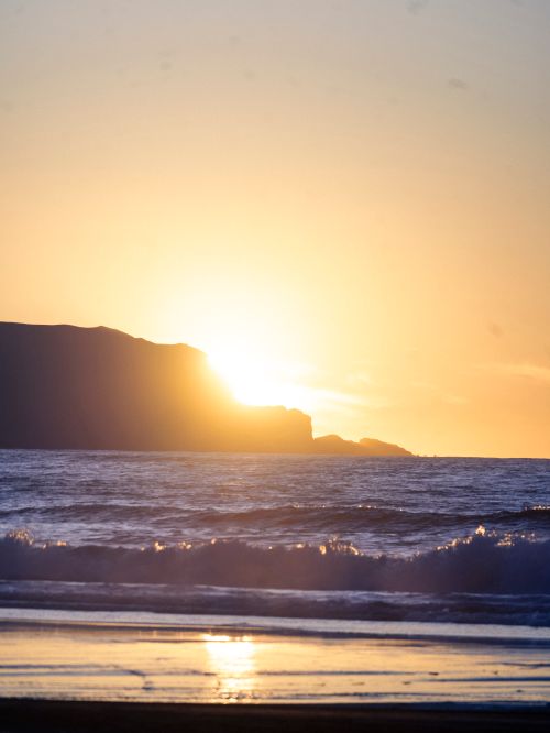 Free A tranquil sunset over the ocean with waves gently hitting the sandy shore. Stock Photo