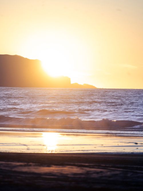 Free Captivating view of the ocean waves at sunset with a golden sky and distant cliff. Stock Photo