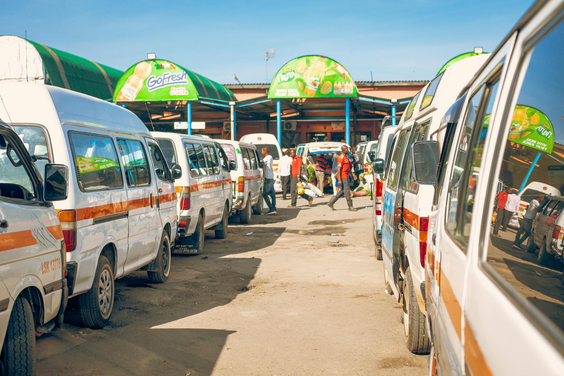 A busy outdoor market scene with white vans lined up under a clear blue sky.