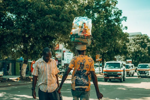 Two men walking down a street with a basket on their heads