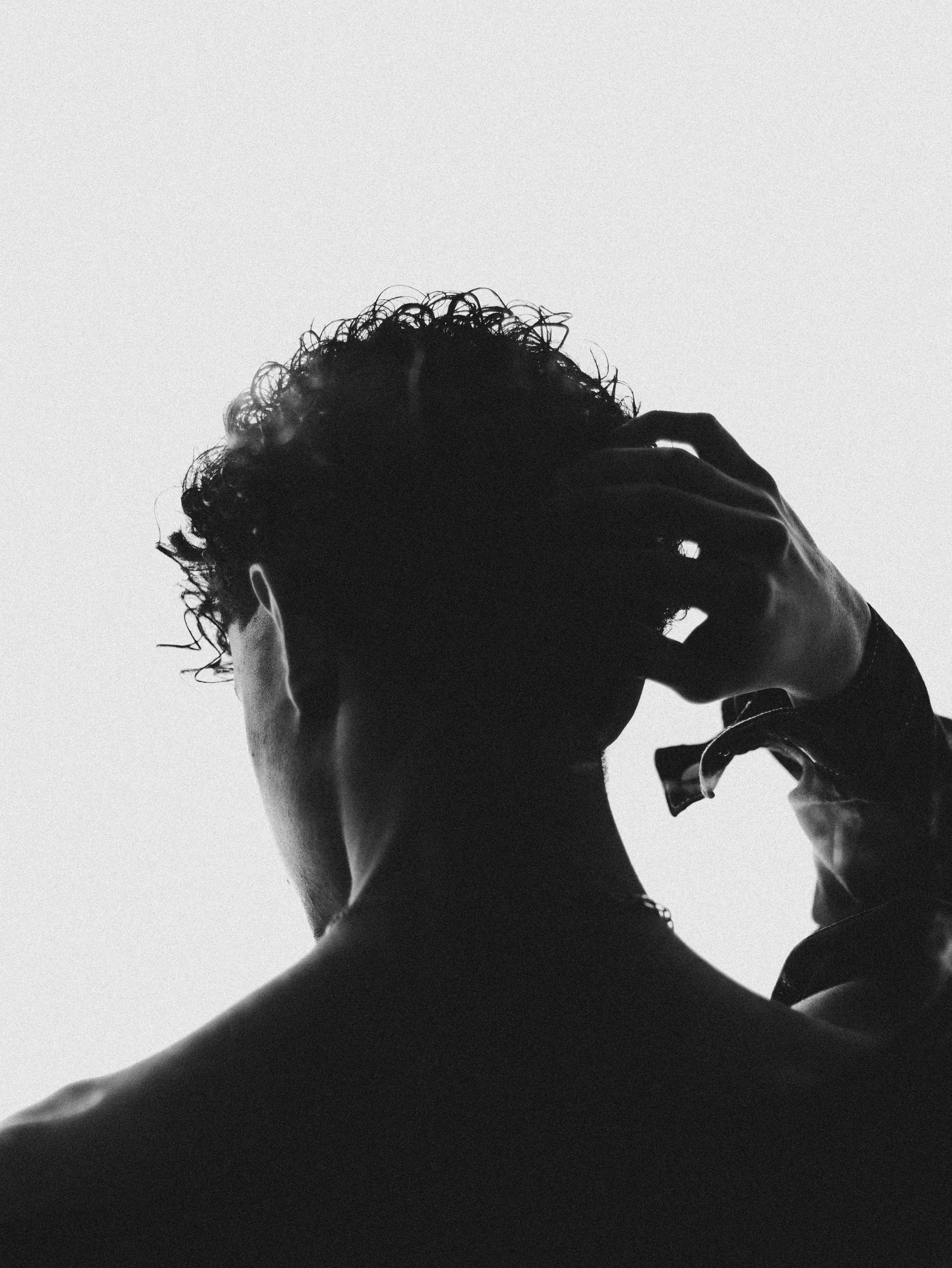 Artistic black and white silhouette of a man scratching his head, emphasizing texture and emotion.