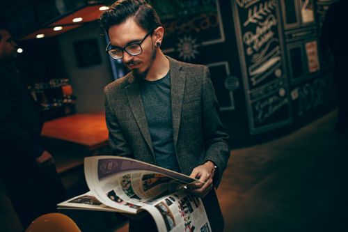 Free A man in a brown blazer reads a magazine in a dimly lit café. Stock Photo