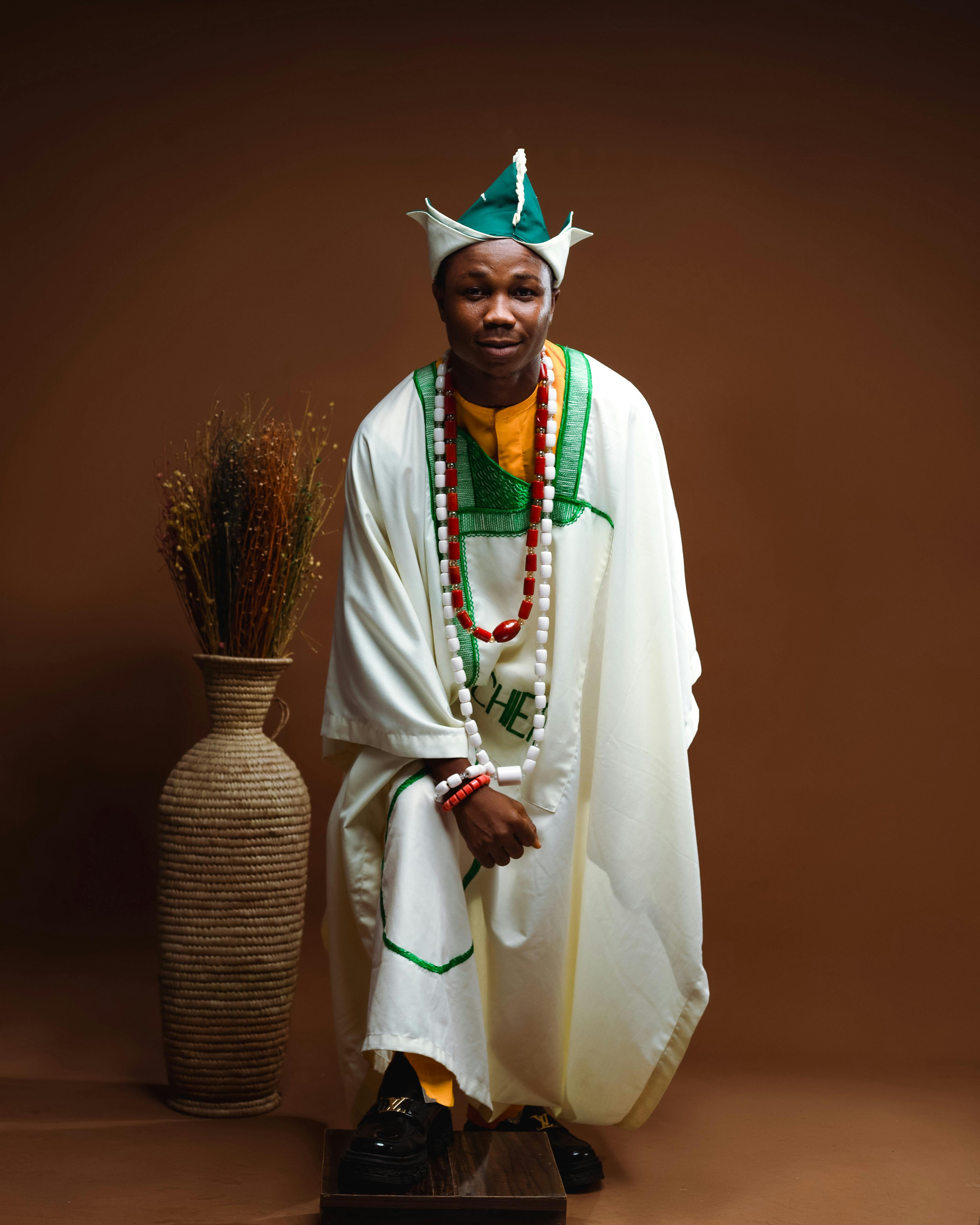 Portrait of a man in traditional Nigerian attire posing in a studio with a cultural backdrop.