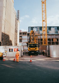 City construction site featuring worker, machinery, and urban surroundings in progress under bright daylight.