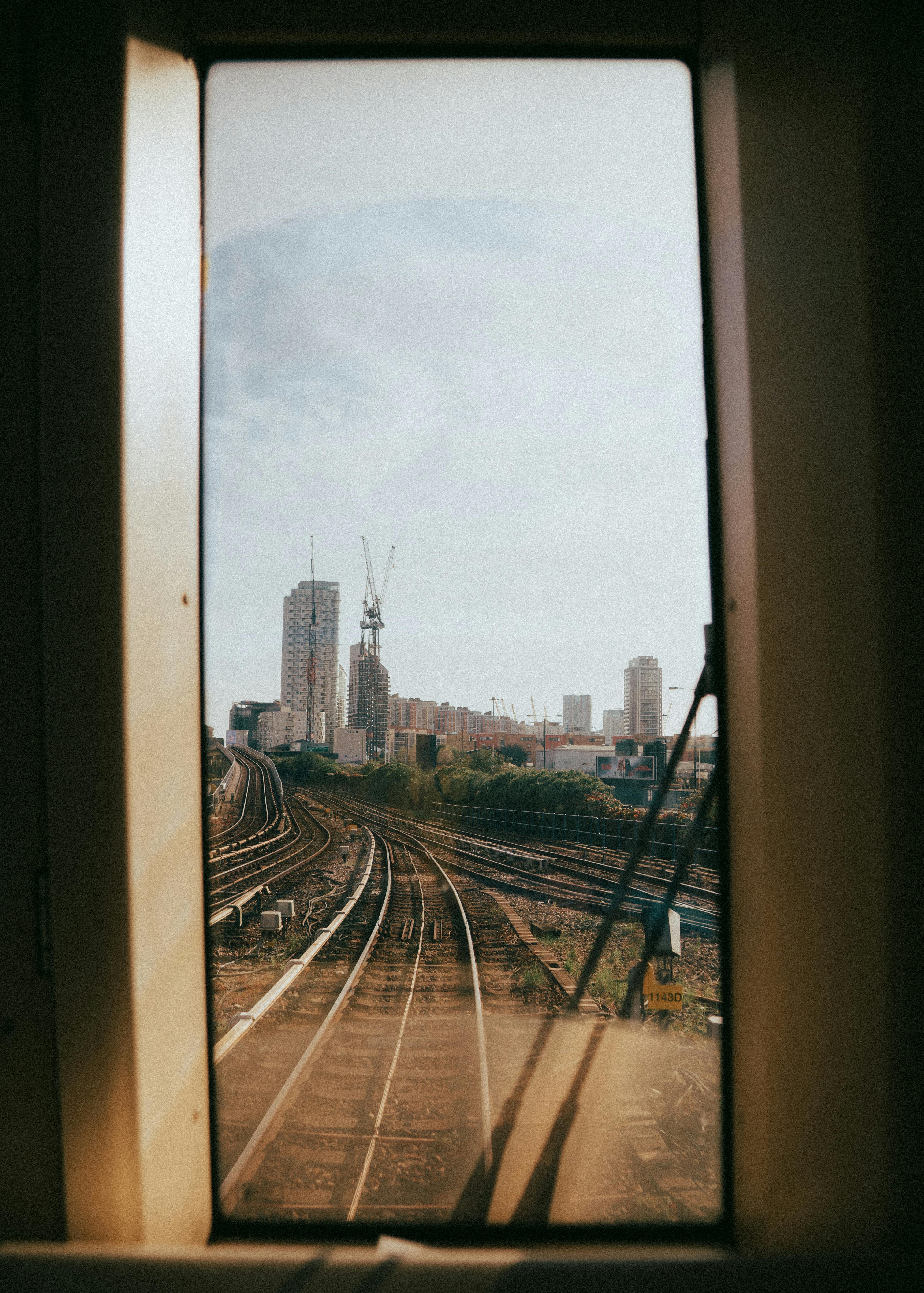 A view of railway tracks leading to a cityscape seen through a train window.