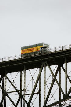 Industrial truck crosses an iron bridge under a cloudy sky, depicting transportation and infrastructure.