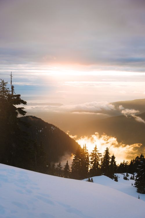 Free Stunning winter landscape of snow-capped mountains and serene forest bathed in sunset light. Stock Photo