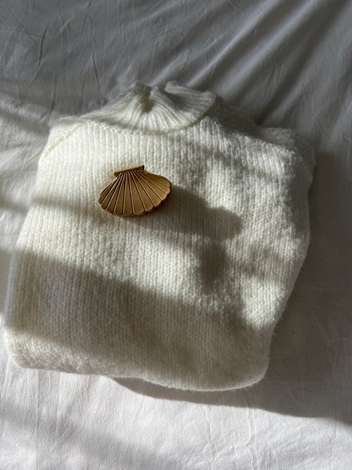 Free Folded white sweater with gold shell clip on a soft fabric background. Stock Photo