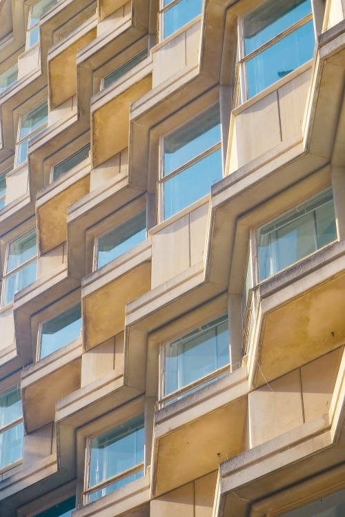 Free Close-up of a modern building facade featuring geometric design and glass windows in a city setting. Stock Photo
