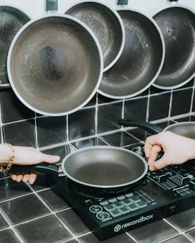 Hands positioned to lift a frying pan from an electric stove in a modern kitchen.