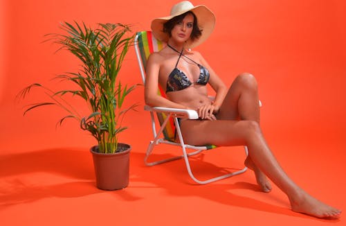 Model in Bikini and Sun Hat Sitting on a Deckchair in the Studio