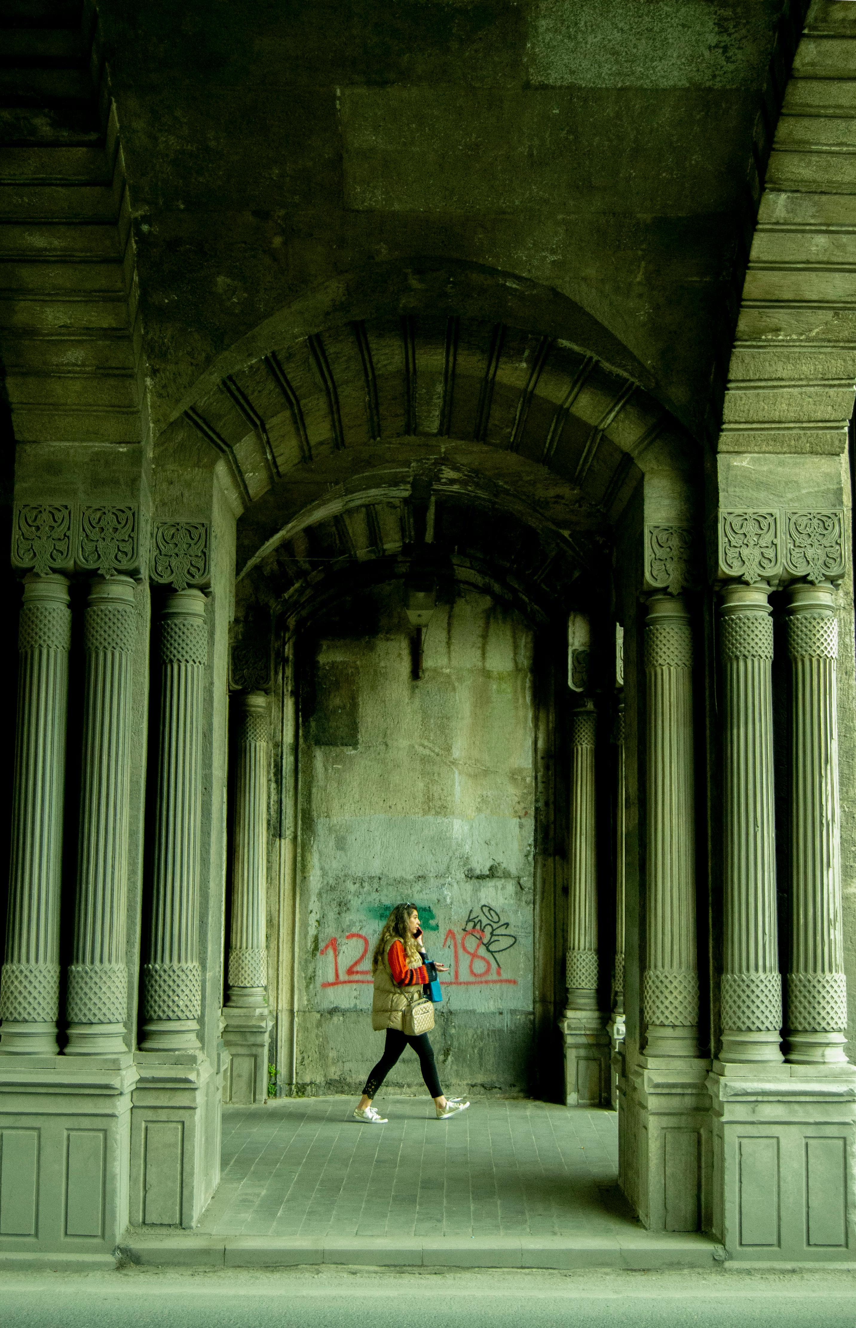A woman walks through an ancient colonnade, capturing urban exploration.
