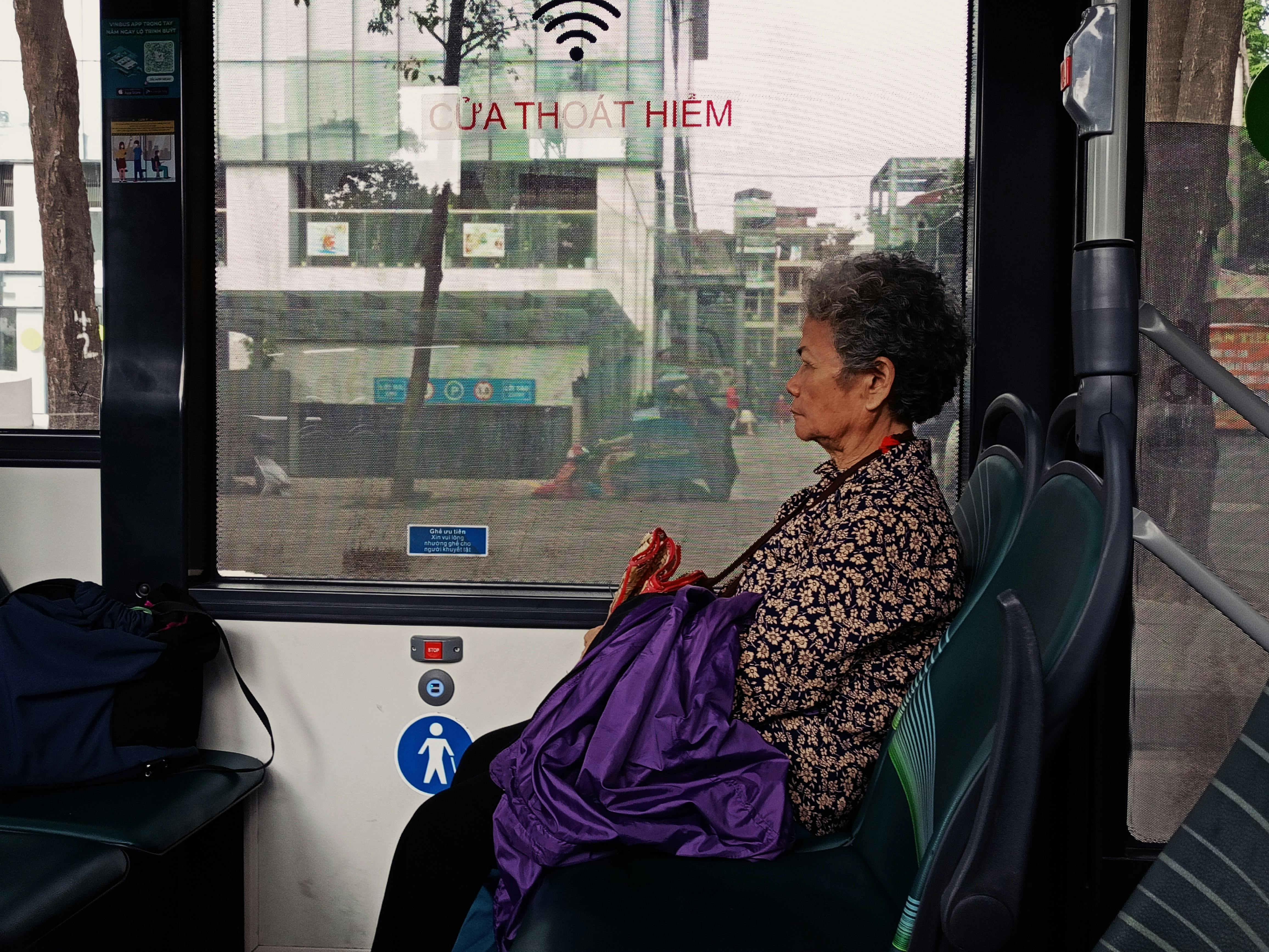 Elderly woman seated on a city bus, reflecting on urban life during a daytime commute.