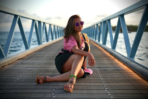 A woman sitting on a wooden pier with sunglasses