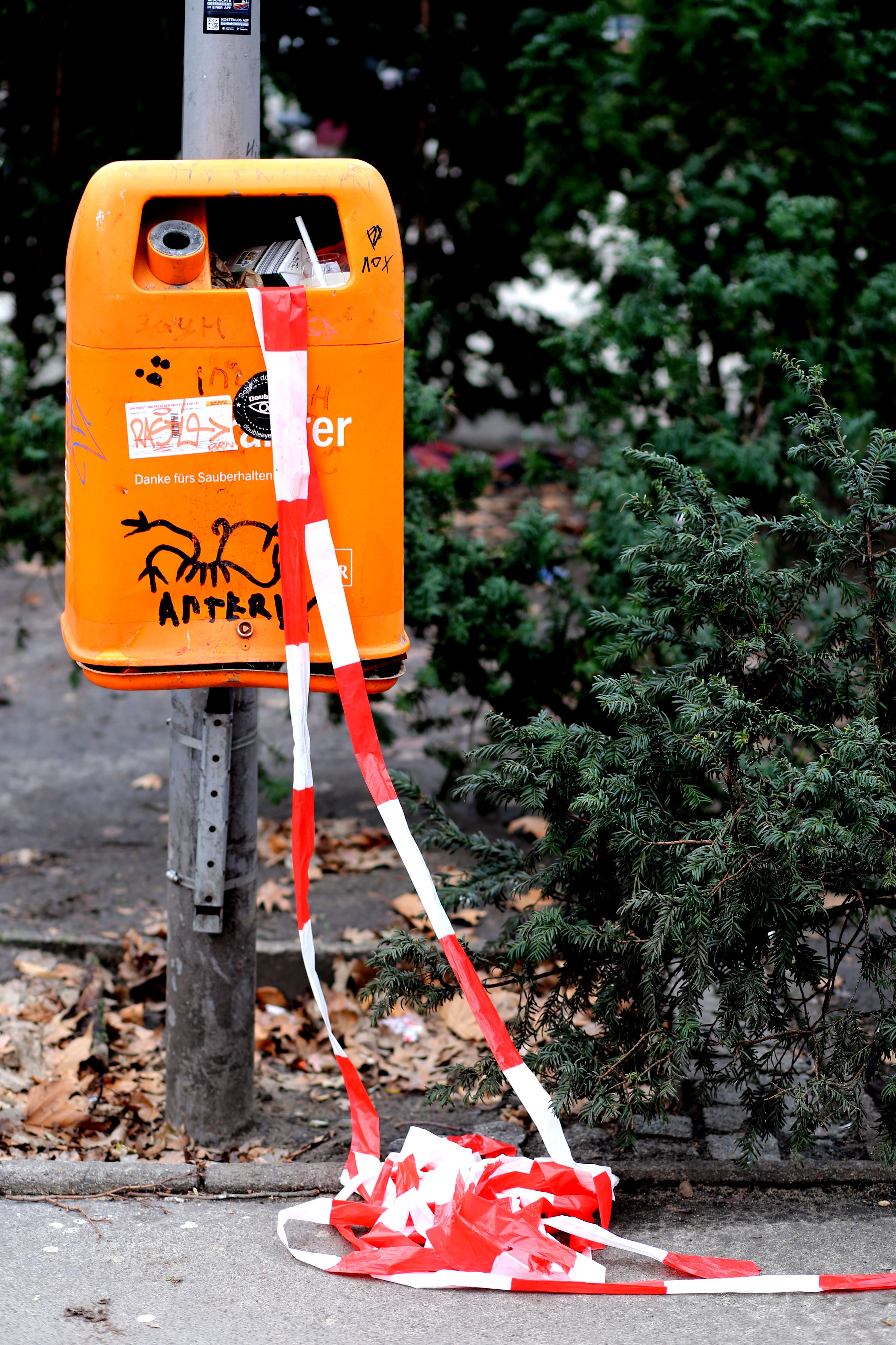 A vibrant urban street scene in Berlin featuring an orange trash bin with graffiti and red tape.