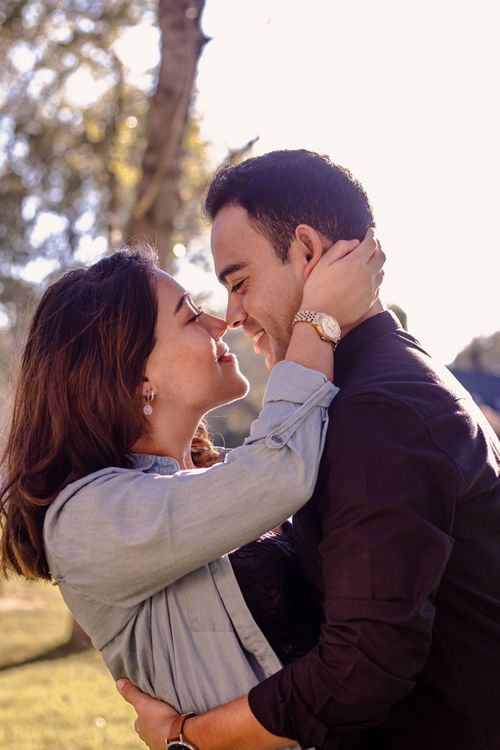 Free Couple embracing outdoors with sunlight and greenery, evoking romance and happiness. Stock Photo