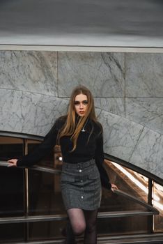 Fashionable woman in a wool skirt and black top posing against a marble wall in the city.