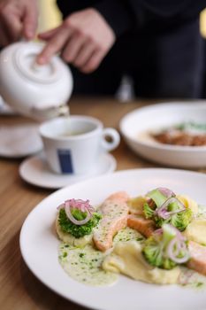 A gourmet salmon dish served with vibrant vegetables and tea in a cozy indoor setting.