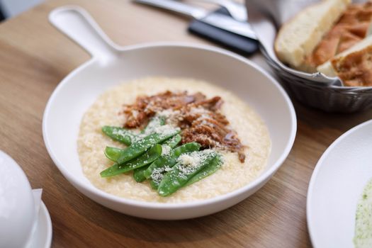Delicious creamy risotto topped with tender snow peas and savory meat, served in a ceramic dish.