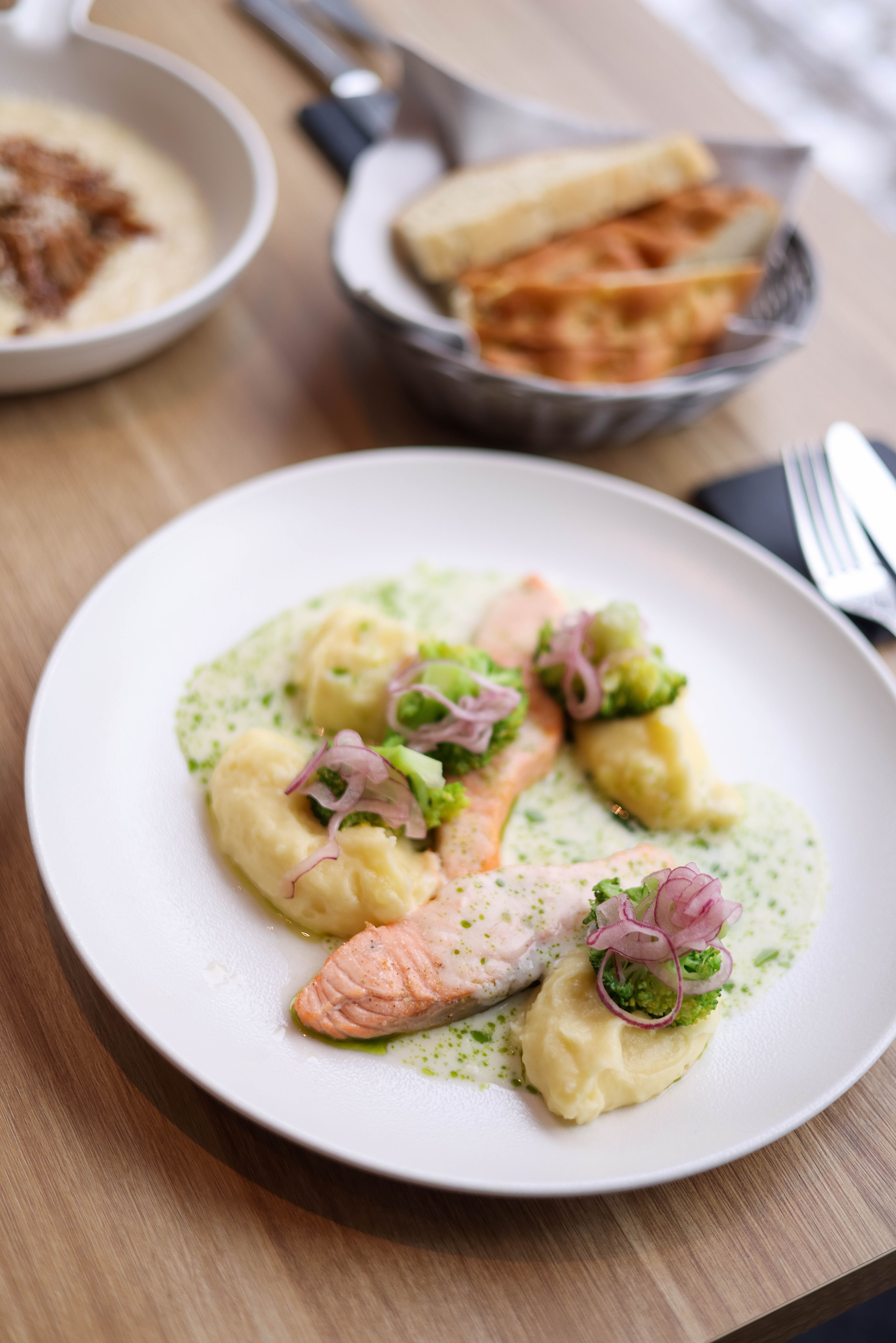 Delicious gourmet salmon with mashed potatoes and greens on a plate with bread in the background.
