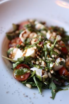 Close-up of a vibrant Caprese salad featuring cherry tomatoes, mozzarella, pesto, and pine nuts.