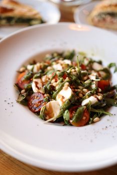 Delicious Caprese salad with cherry tomatoes, mozzarella, arugula, and pine nuts in a white bowl.