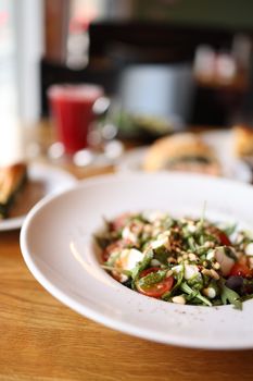 Close-up of a fresh arugula salad with tomatoes and pine nuts on a white plate indoors.