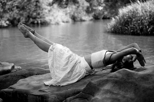 Free Woman Lying And Stretching On Rock Beside Body Of Water Stock Photo