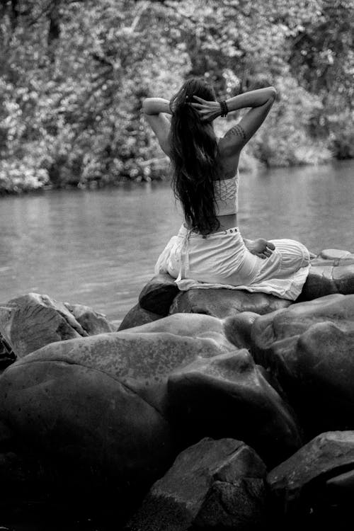 Женщина, сидящая на скале, держась за голову у водоема