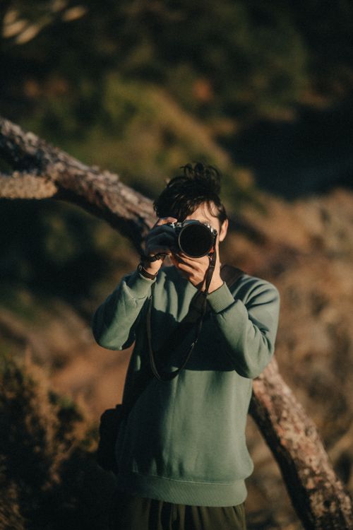 Free A young photographer takes pictures outdoors in warm, natural lighting. Stock Photo