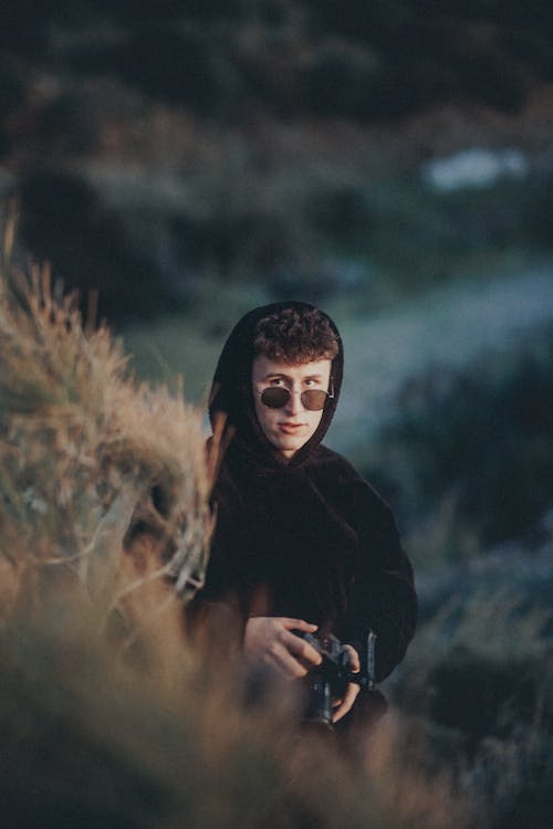 A young man in a hoodie and sunglasses is holding a camera