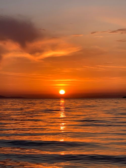 Free Stunning sunset over the tranquil Ayvalık coastline in Türkiye with vibrant orange hues. Stock Photo