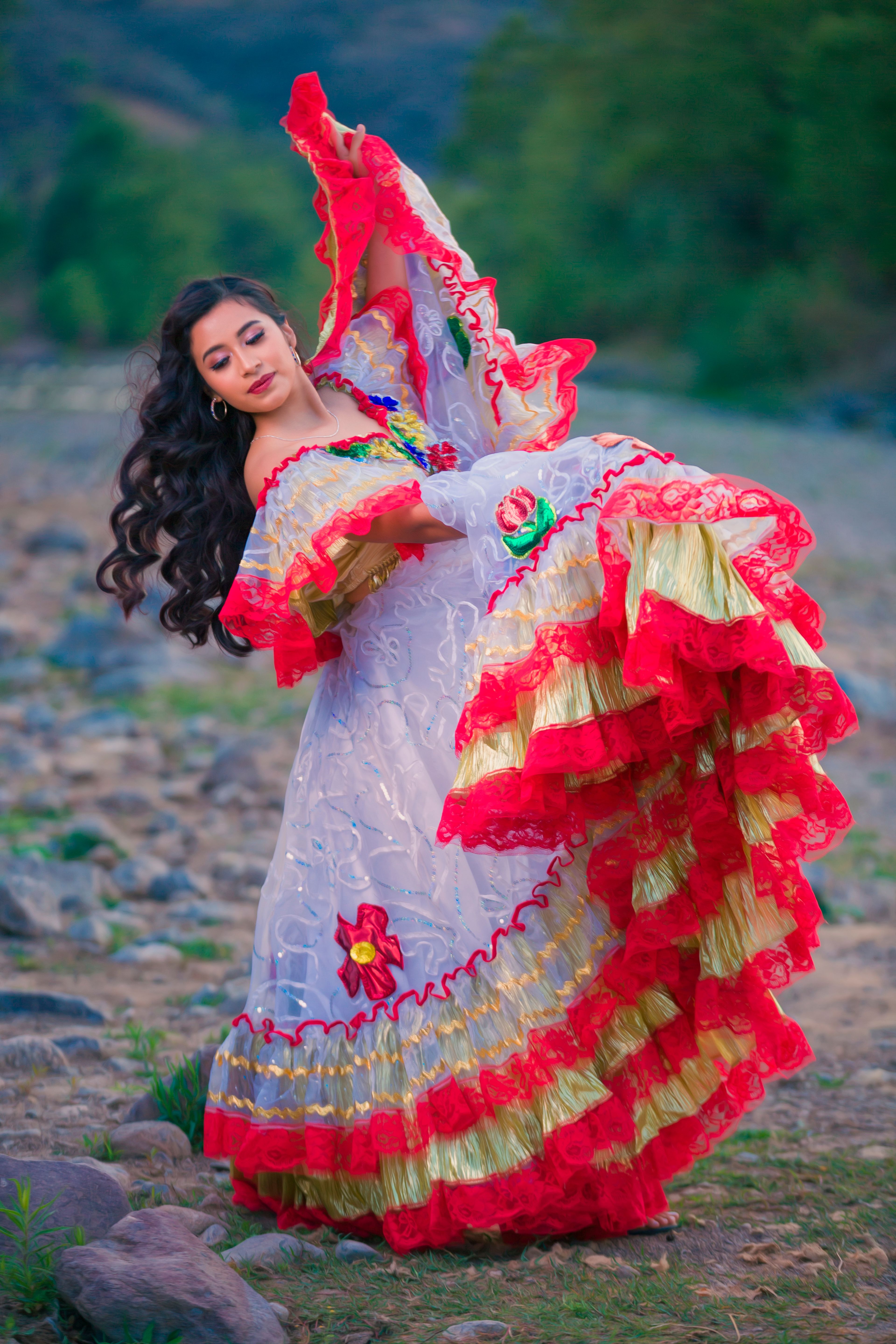 A woman in vibrant traditional Mexican attire dances gracefully in a serene outdoor setting.