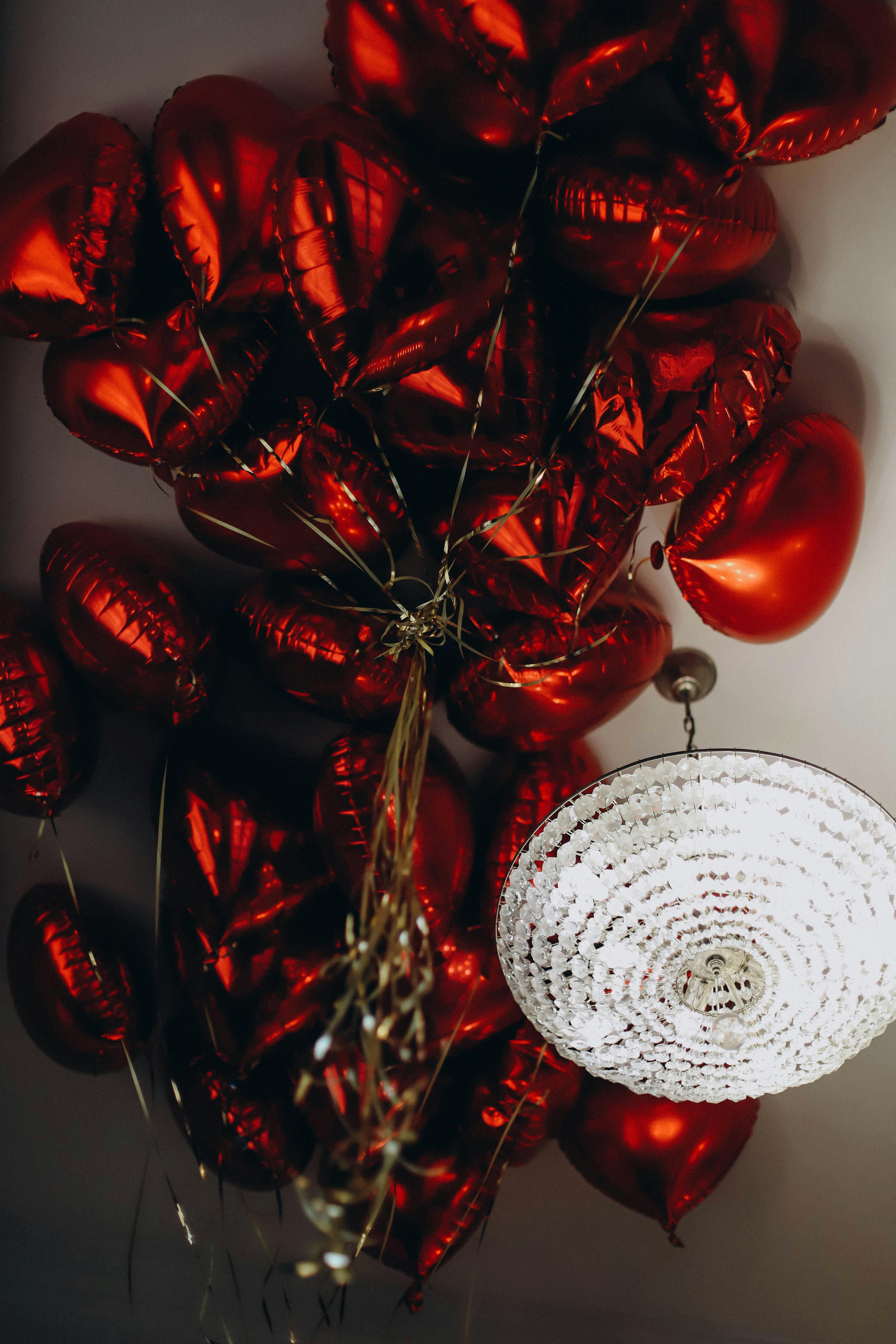 Cluster of red heart-shaped balloons with chandelier on white ceiling, perfect for celebrations.