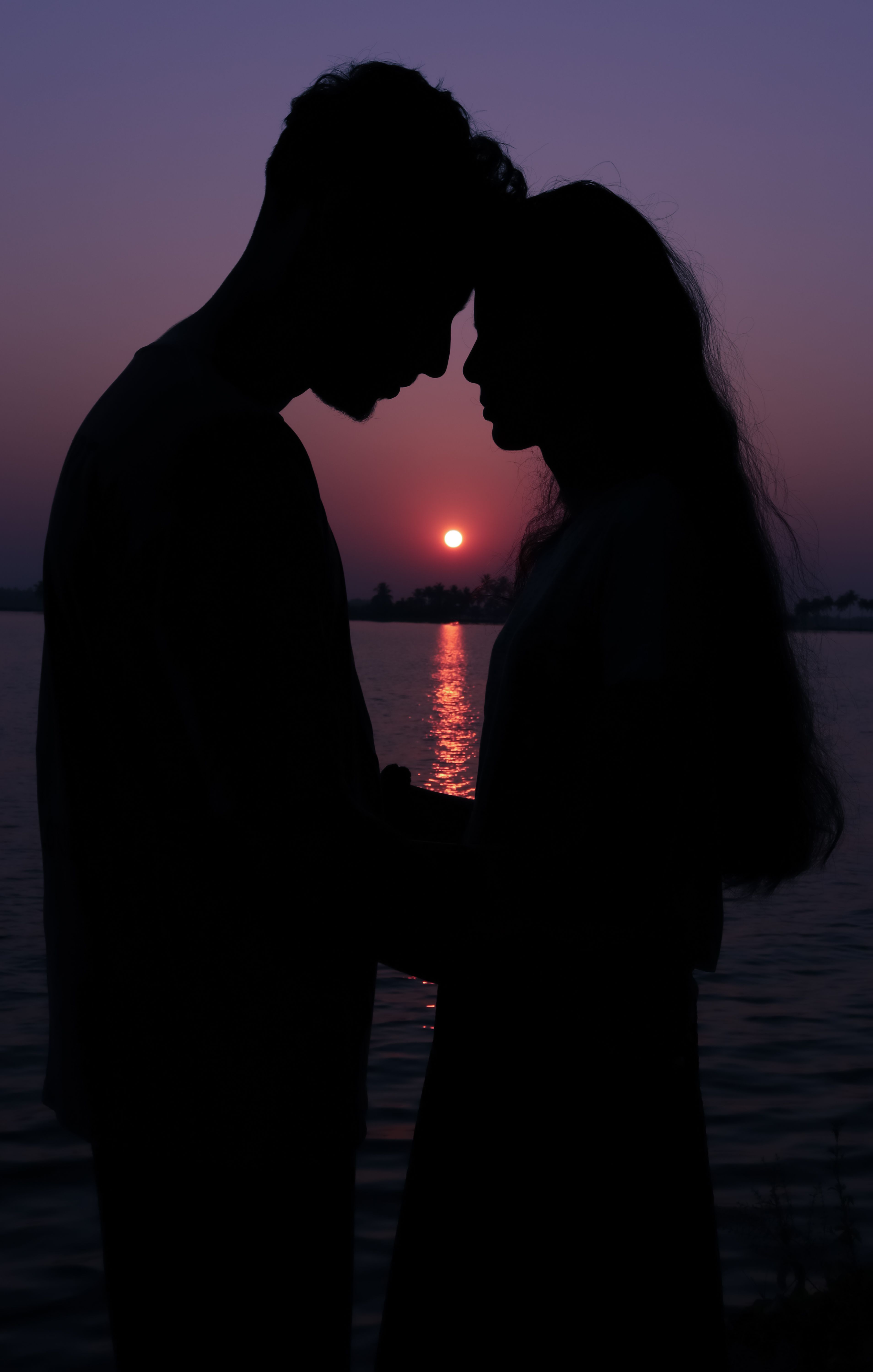 A couple stands head to head, silhouetted against a beautiful sunset in Pullinkunnu, India.