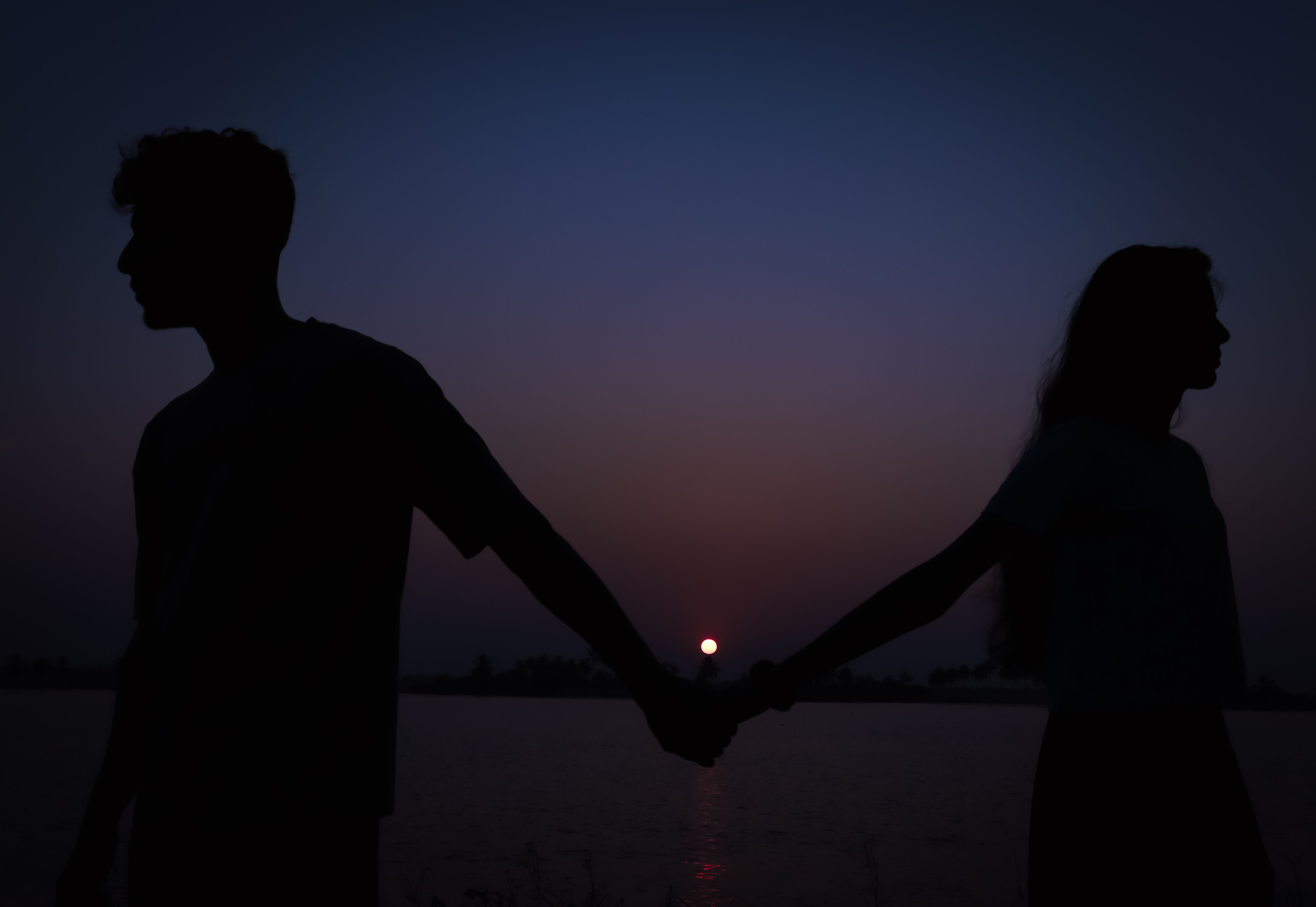 Silhouette of a Couple Holding Hands by a Body of Water at Sunset ...