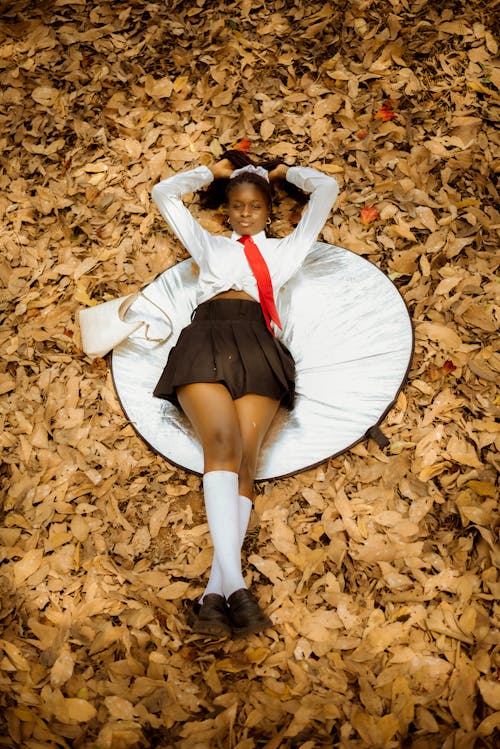 Girl Lying Down in White Shirt with Tie and in Skirt on Autumn Leaves
