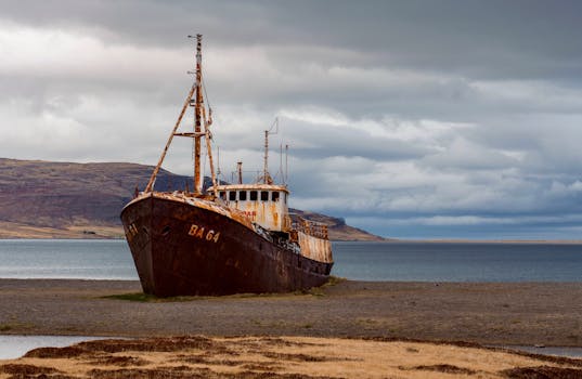 Abandoned rusted shipwreck BA 64 on Iceland's deserted coast under dramatic cloudy sky.
