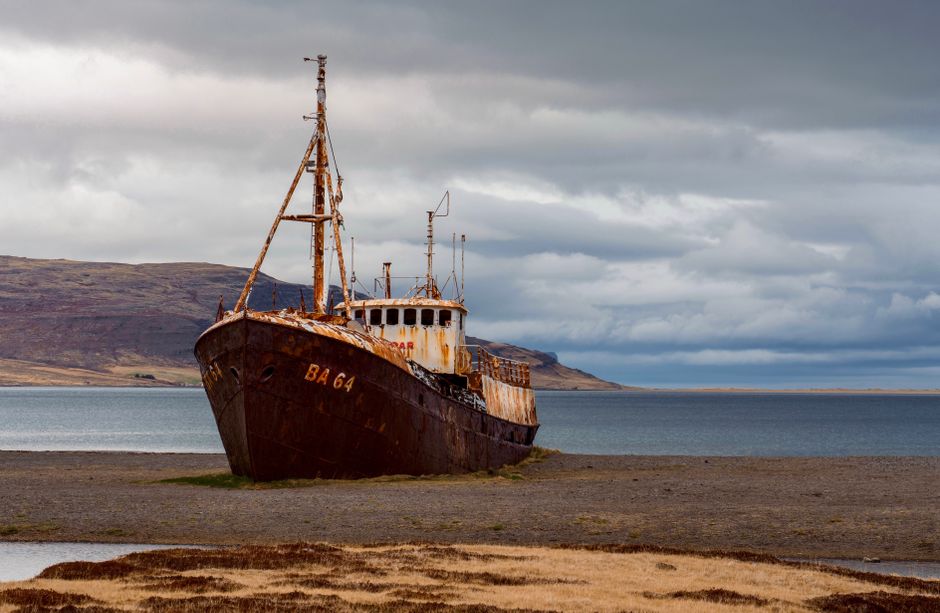 Abandoned rusted shipwreck BA 64 on Iceland's deserted coast under dramatic cloudy sky.