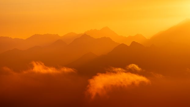 Stunning view of sunset over the Alps with misty layers and vibrant orange hues.
