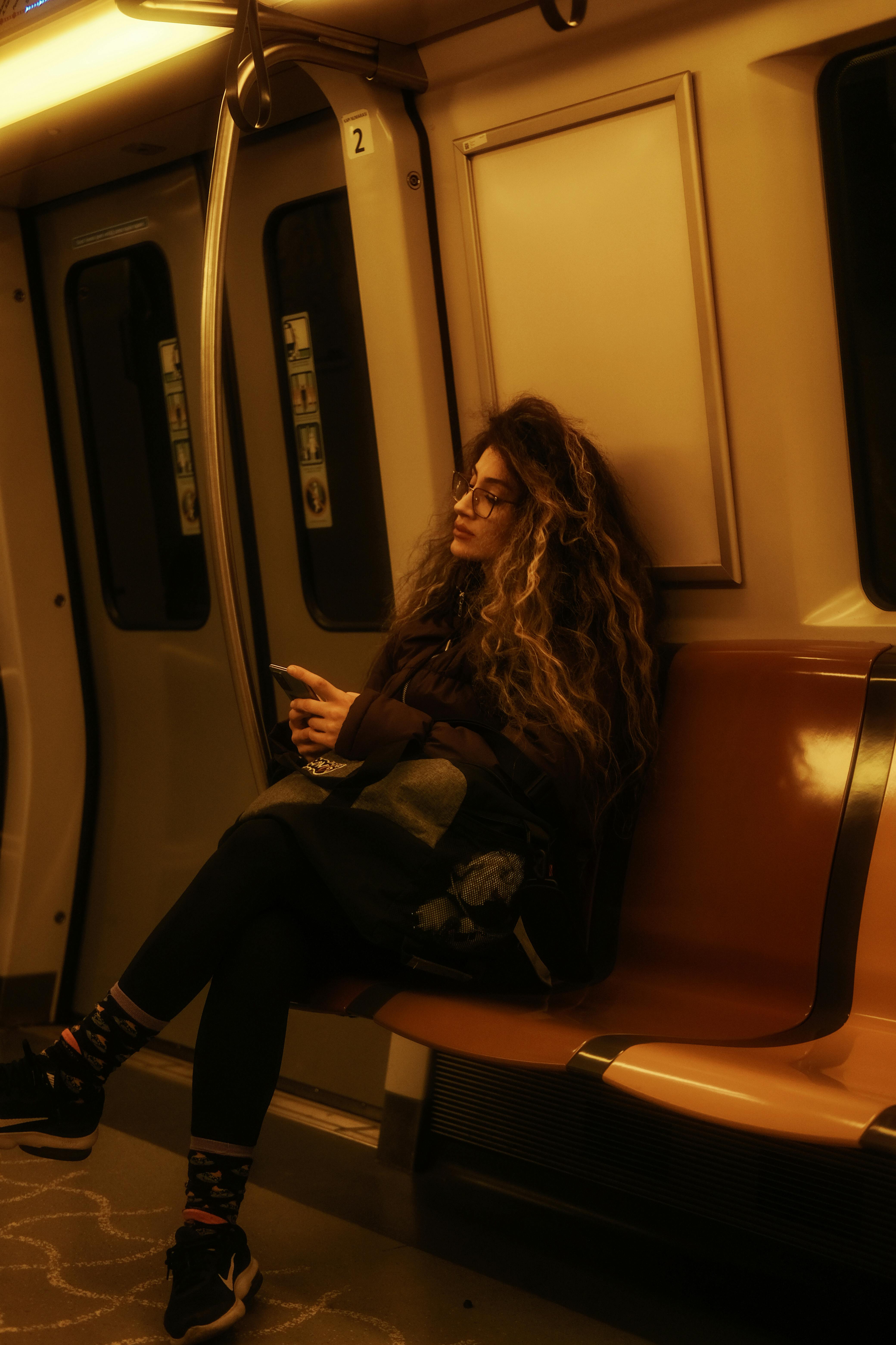 A woman with curly hair uses a smartphone while sitting on a train seat.