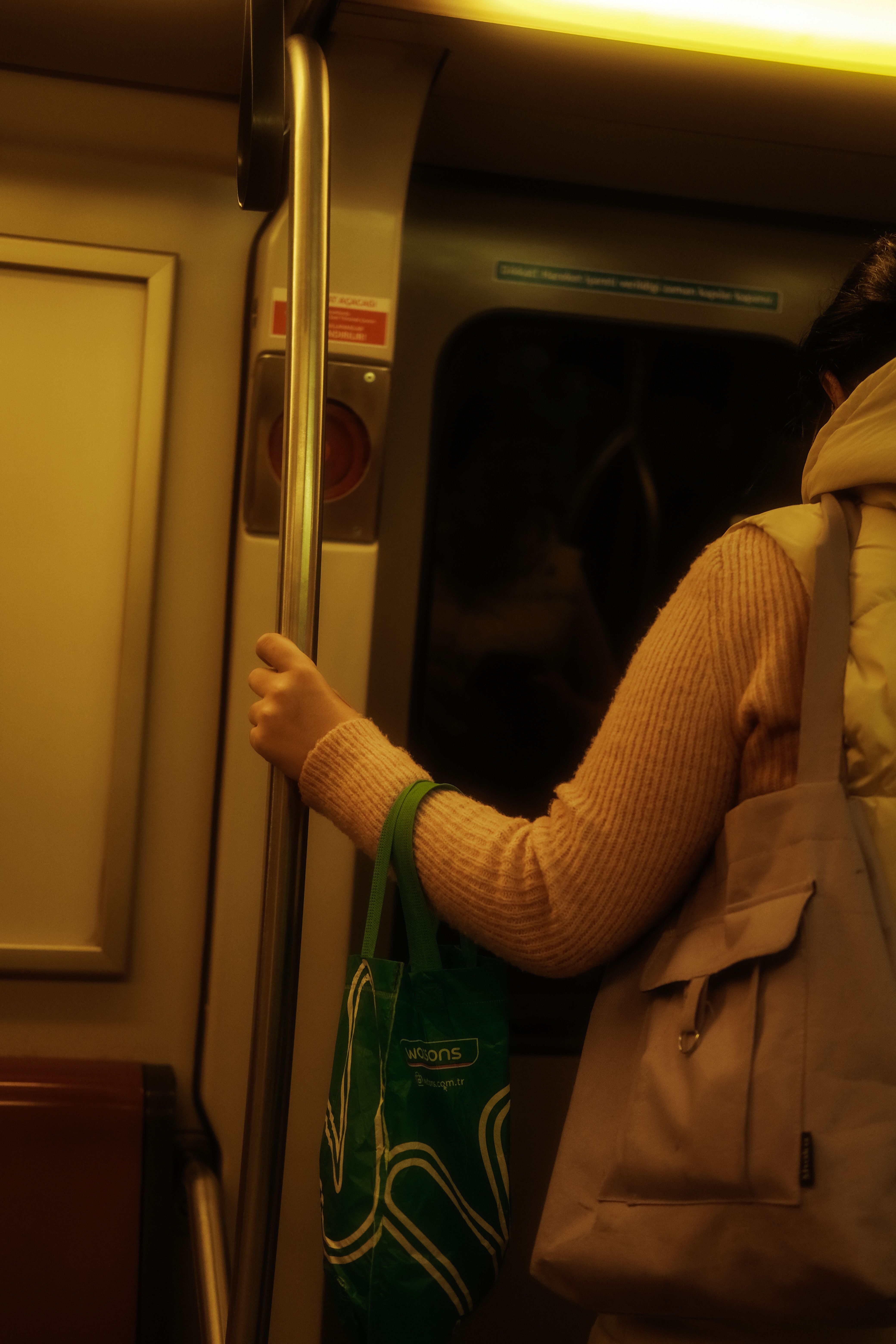A woman standing in a metro train holding onto a handrail with shopping bags.